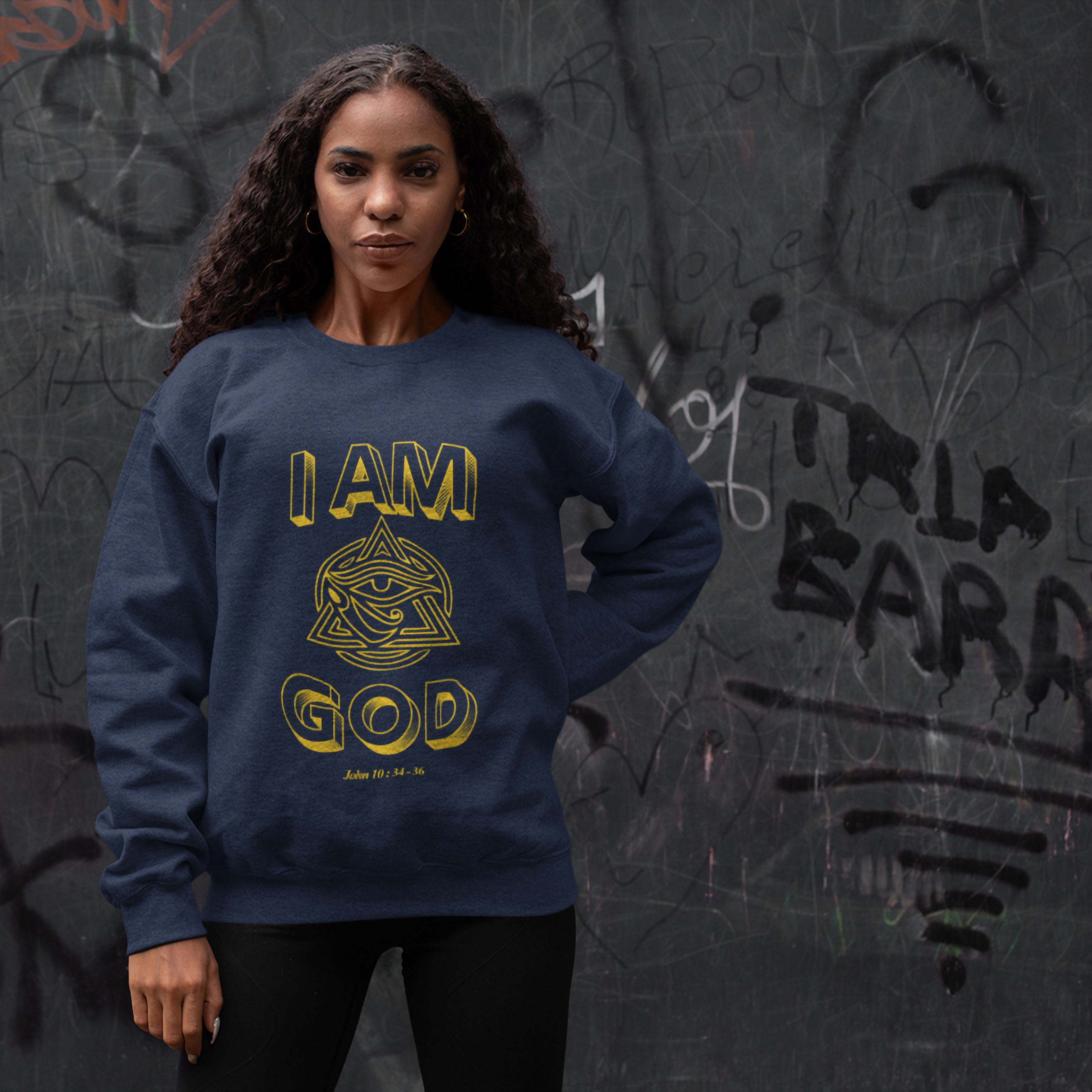 Woman wearing a blue sweatshirt with 'I AM GOD' text against a graffiti-covered wall.
